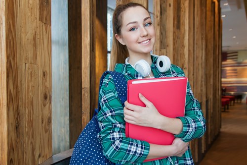 Young person wearing a backpack and carrying books, while smiling