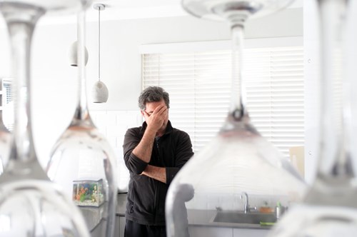 a stressed man stood in front of a row of wine glasses
