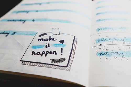 A close up photo of a diary with the words make it happen written in black felt tip pen