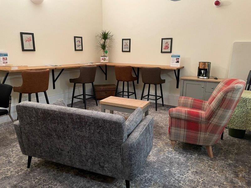 Sofas on a soft carpet, with desk space running along the walls, and pictures on the wall