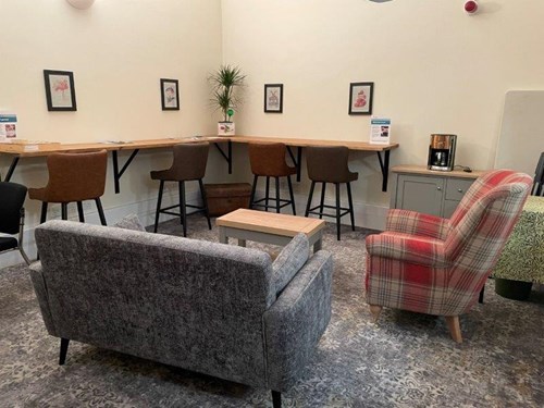 Sofas on a soft carpet, with desk space running along the walls, and pictures on the wall